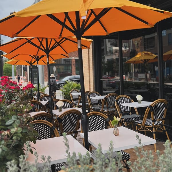 Kiki's Coffee & Spirits outdoor patio with orange umbrellas, white tables, and black and white chairs.