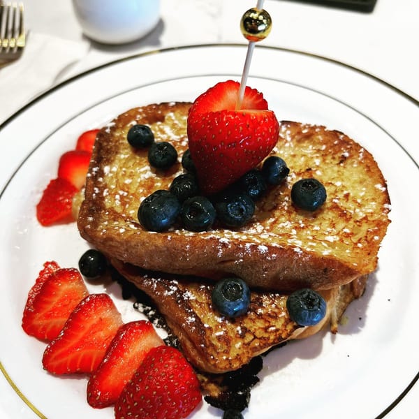 Golden French toast stacked with powdered sugar, blueberries, and sliced strawberries on a white plate.