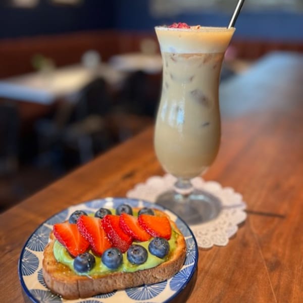 Avocado toast with strawberries and blueberries, next to an iced coffee drink on a wooden table.