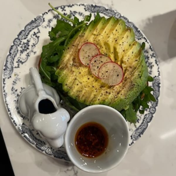 Avocado toast with sliced radishes and black pepper, served with a side of sauce.