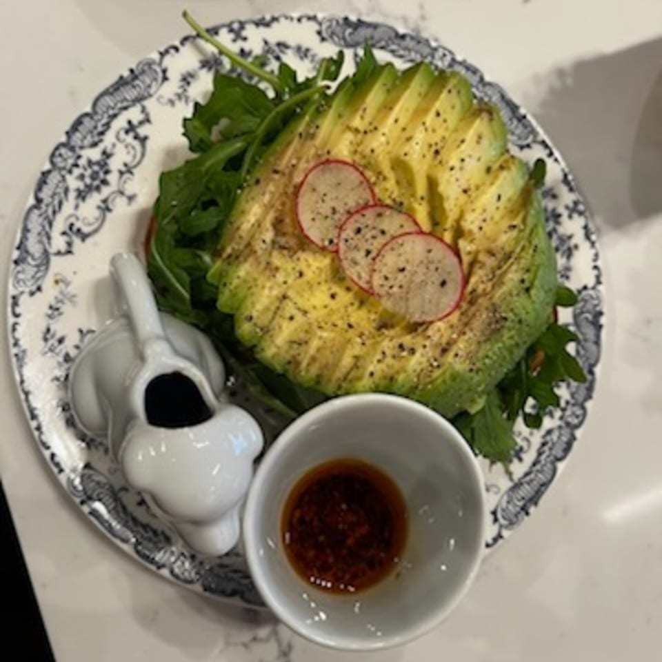 Avocado toast with sliced radishes and black pepper, served with a side of sauce.