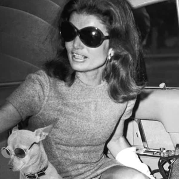 Black and white photo of a woman in sunglasses with a small dog also wearing sunglasses.