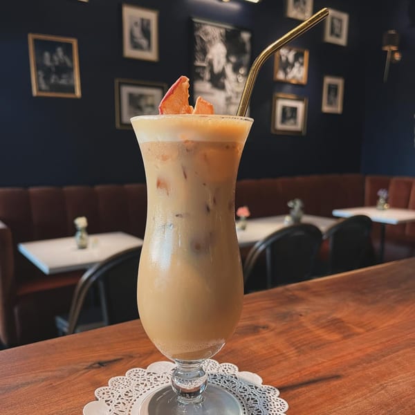 Iced coffee with foam and dried fruit garnish, served in a tall glass with a gold straw.