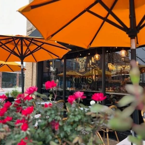 Kiki's Coffee & Spirits patio with orange umbrellas, red flowers, and the Kiki's logo on the window.