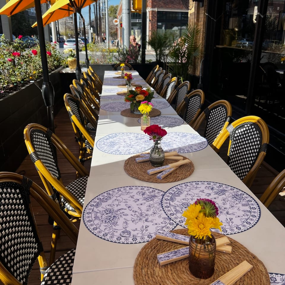 Long outdoor dining table at Kiki's Coffee & Spirits, set with placemats, flowers, and fans.