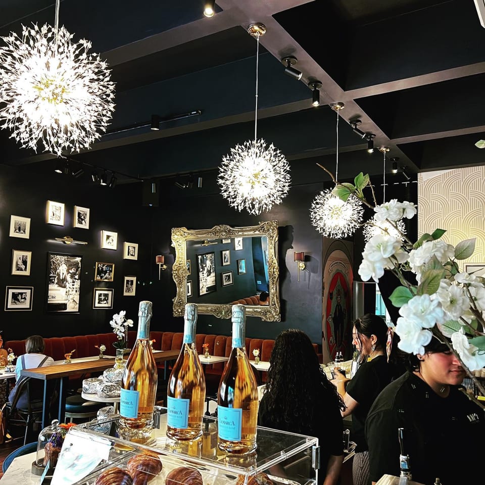 Kiki's Coffee & Spirits interior with sparkling chandeliers, framed photos, and bottles of rosé on the counter.