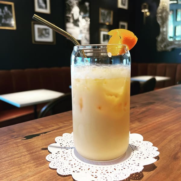 A Kiki's Coffee & Spirits iced coffee with orange garnish and metal straw on a wooden table.