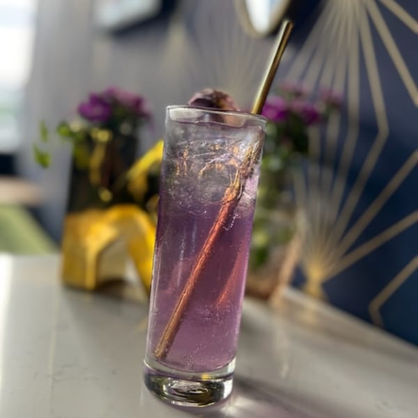 A tall glass of purple Kiki's Coffee & Spirits cocktail with ice and a gold straw.