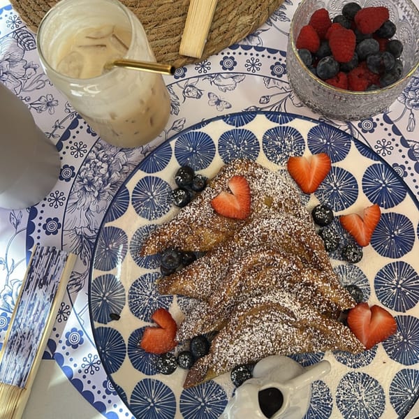 French toast with powdered sugar, heart-shaped strawberries, blueberries, and an iced coffee.