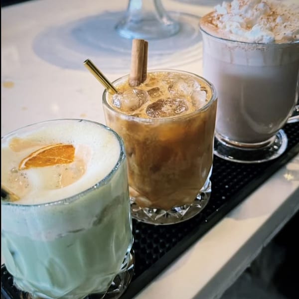 Three Kiki's Coffee & Spirits drinks: a green drink with orange, an iced coffee with cinnamon, and a latte.