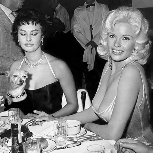 Black and white photo of Sophia Loren with a chihuahua, and Jayne Mansfield smiling at a table.
