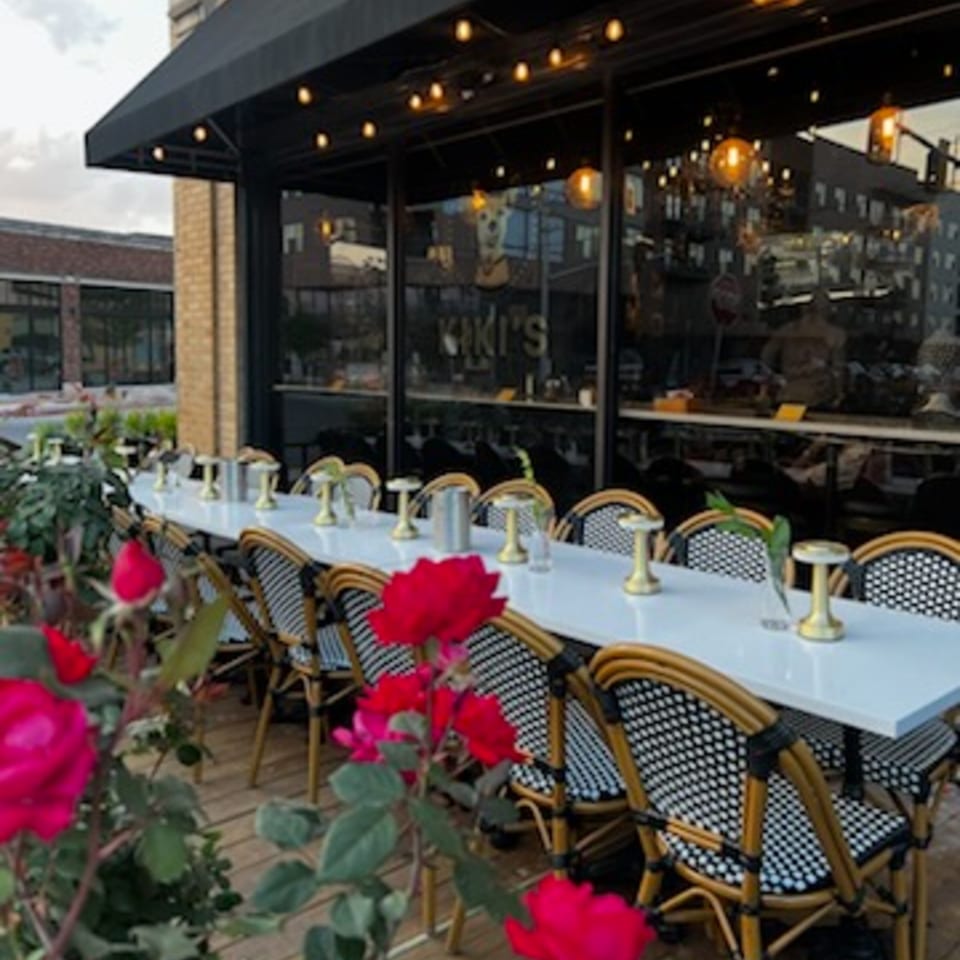 Outdoor patio of Kiki's Coffee & Spirits with a long table, chairs, and red roses in the foreground.