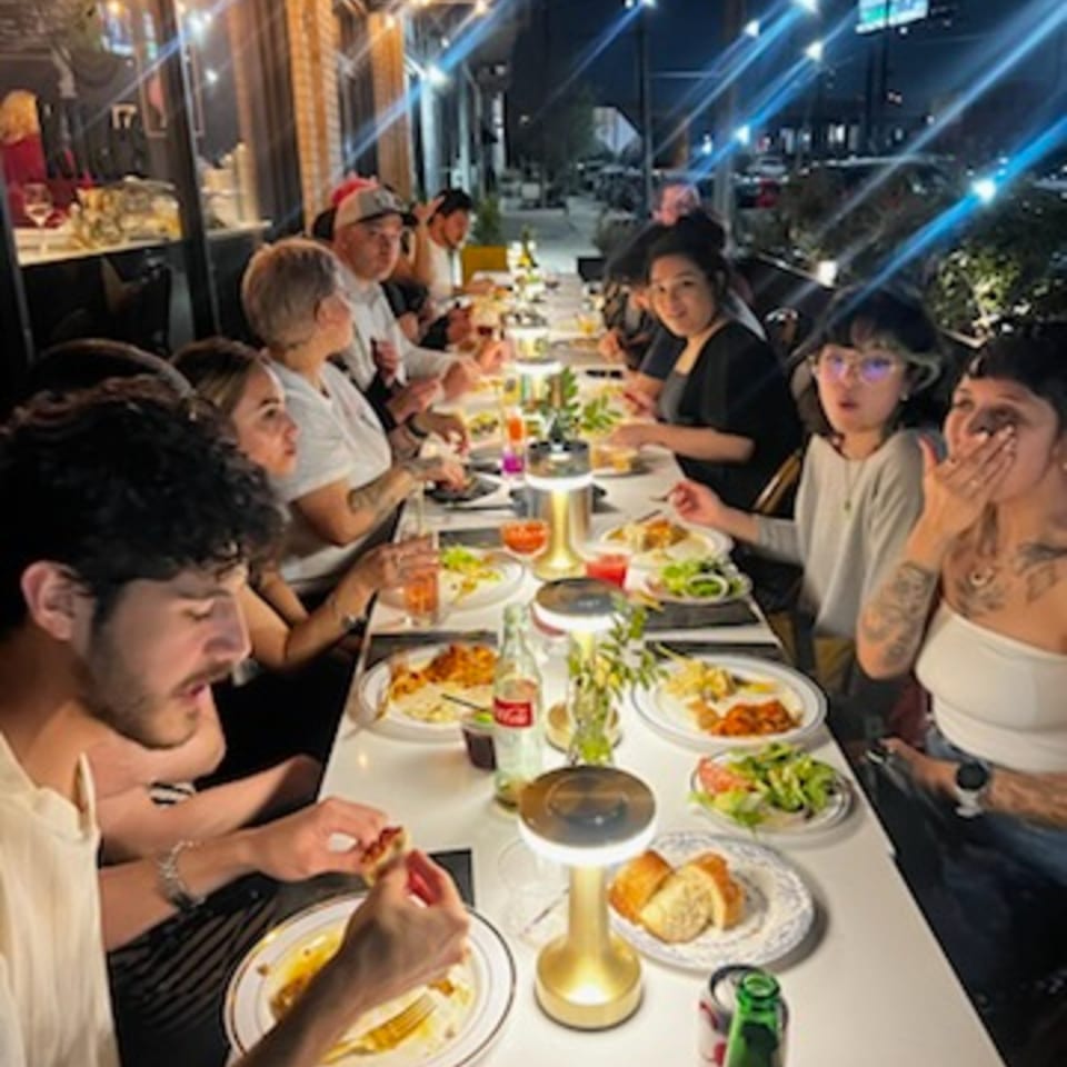 Friends enjoy dinner together at a long table on Kiki's outdoor patio at night.
