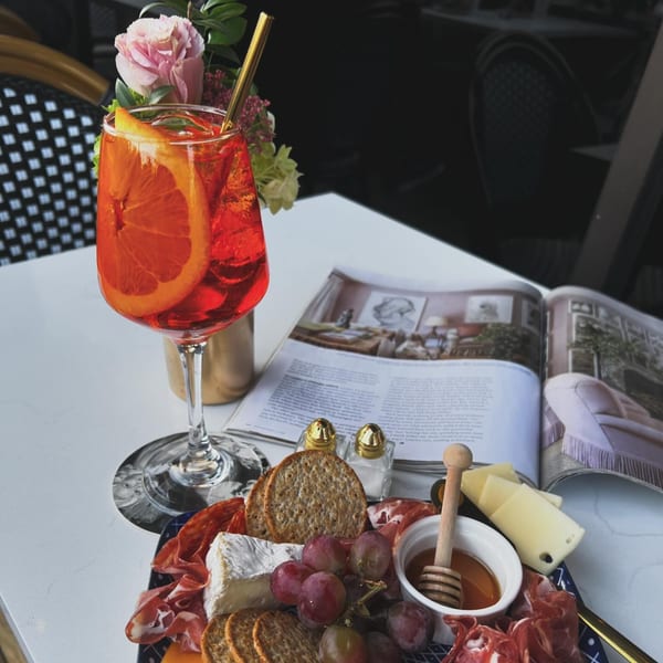 A vibrant orange cocktail with a charcuterie board and an open magazine on a white table.